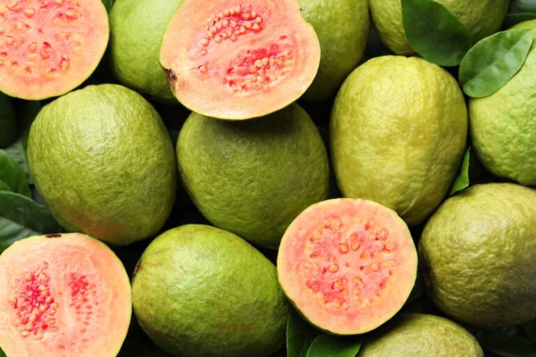 Frutas de guayaba enteras y recién cortadas como fondo, vista desde arriba.